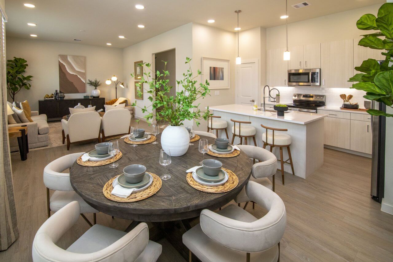 Modern open-concept interior featuring a round dining table, contemporary kitchen with white cabinetry and island seating, and a stylish living area with neutral décor.