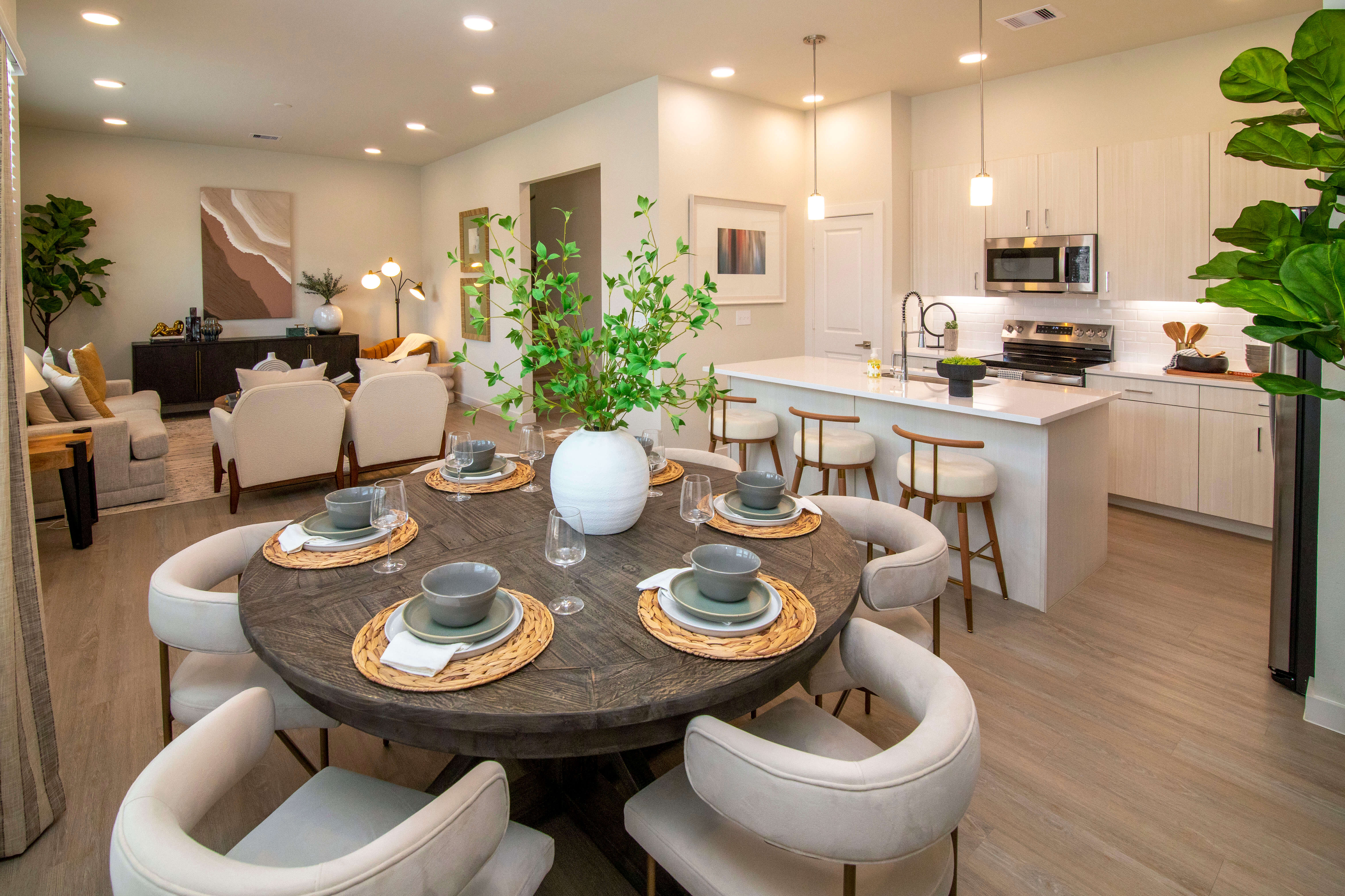 Modern open-concept interior featuring a round dining table, contemporary kitchen with white cabinetry and island seating, and a stylish living area with neutral décor.